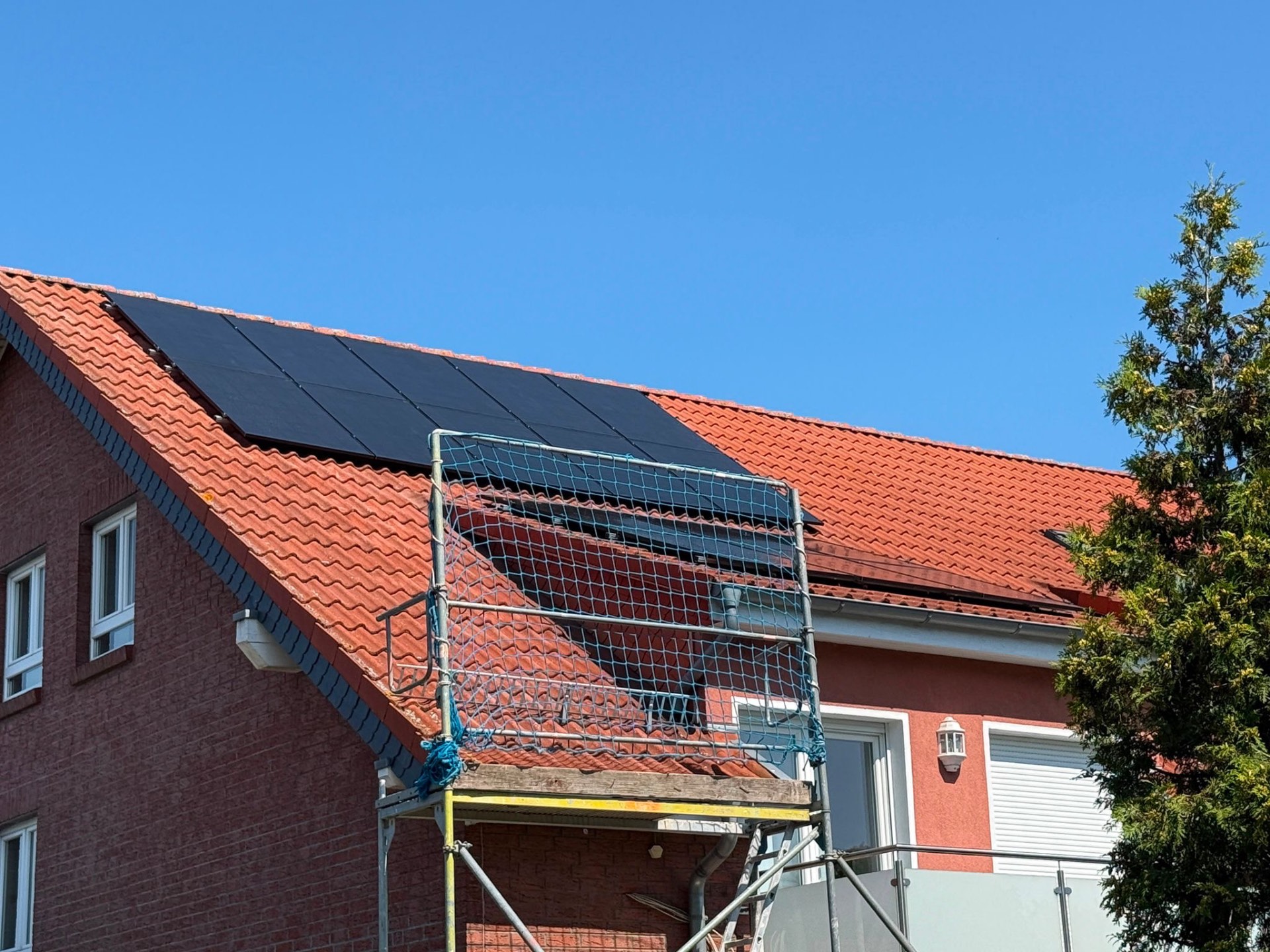 Rotes Ziegeldach mit schwarzen Solarmodulen neben einer Gaube