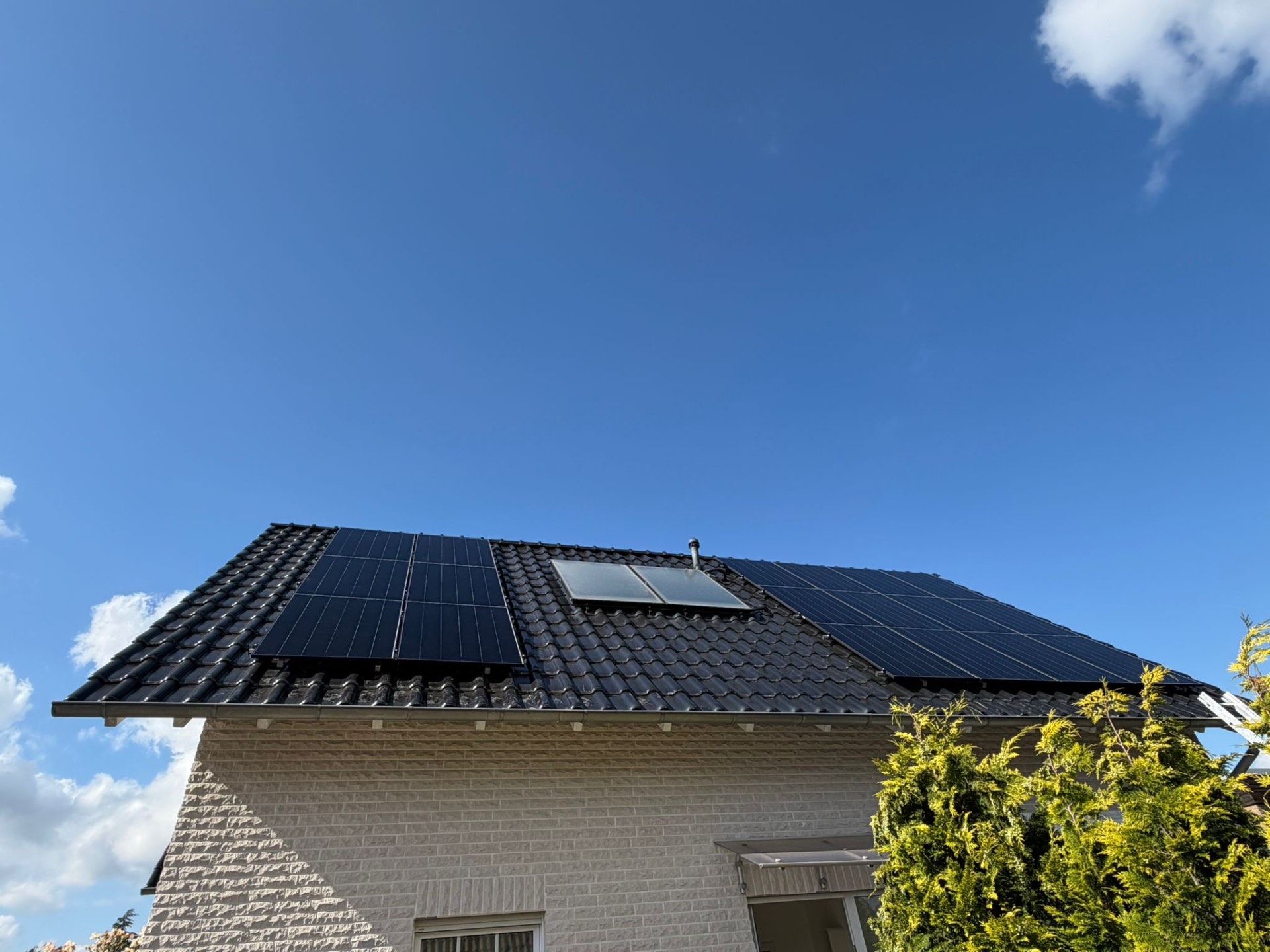 Schwarzes Ziegeldach mit Photovoltaikfeldern und Solarthermie-Kollektor